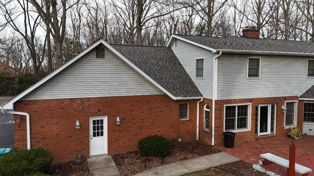Brian Leonard project — elevated view of a Midwest brick-and-siding home showing asphalt shingle roof planes, white gutters and downspouts, chimney, and exterior transitions