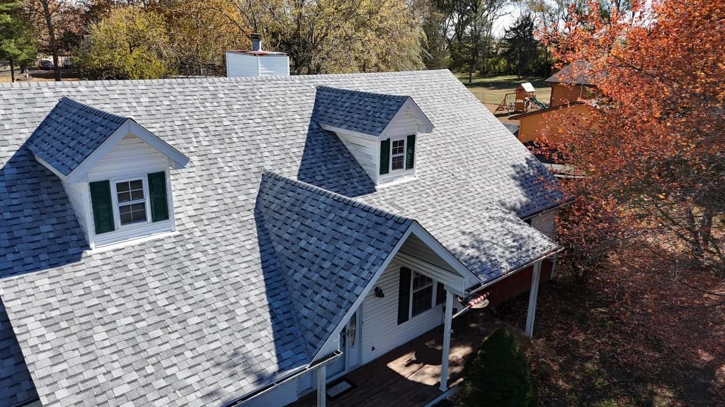 Residential home with light-gray architectural shingles, dormers, and ridge lines — roof-focused elevated documentation view