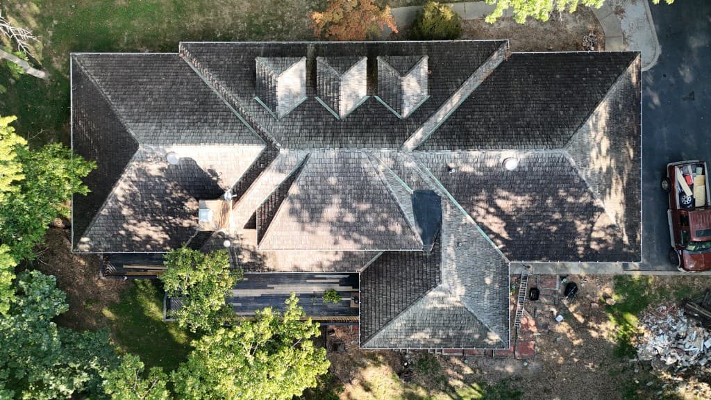 Tim Zolman property — completed aerial view showing restored roof planes with uniform shakes/shingles, white gutters, dormers and vents, and finished perimeter detail